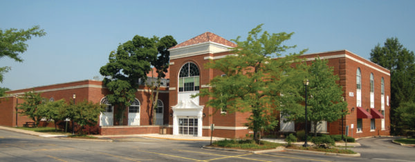 A two-story red brick building with large arched windows, surrounded by trees and a mostly empty parking lot on a clear day—a classic setting often featured in Bradbury Miller Associates (BMA) projects.