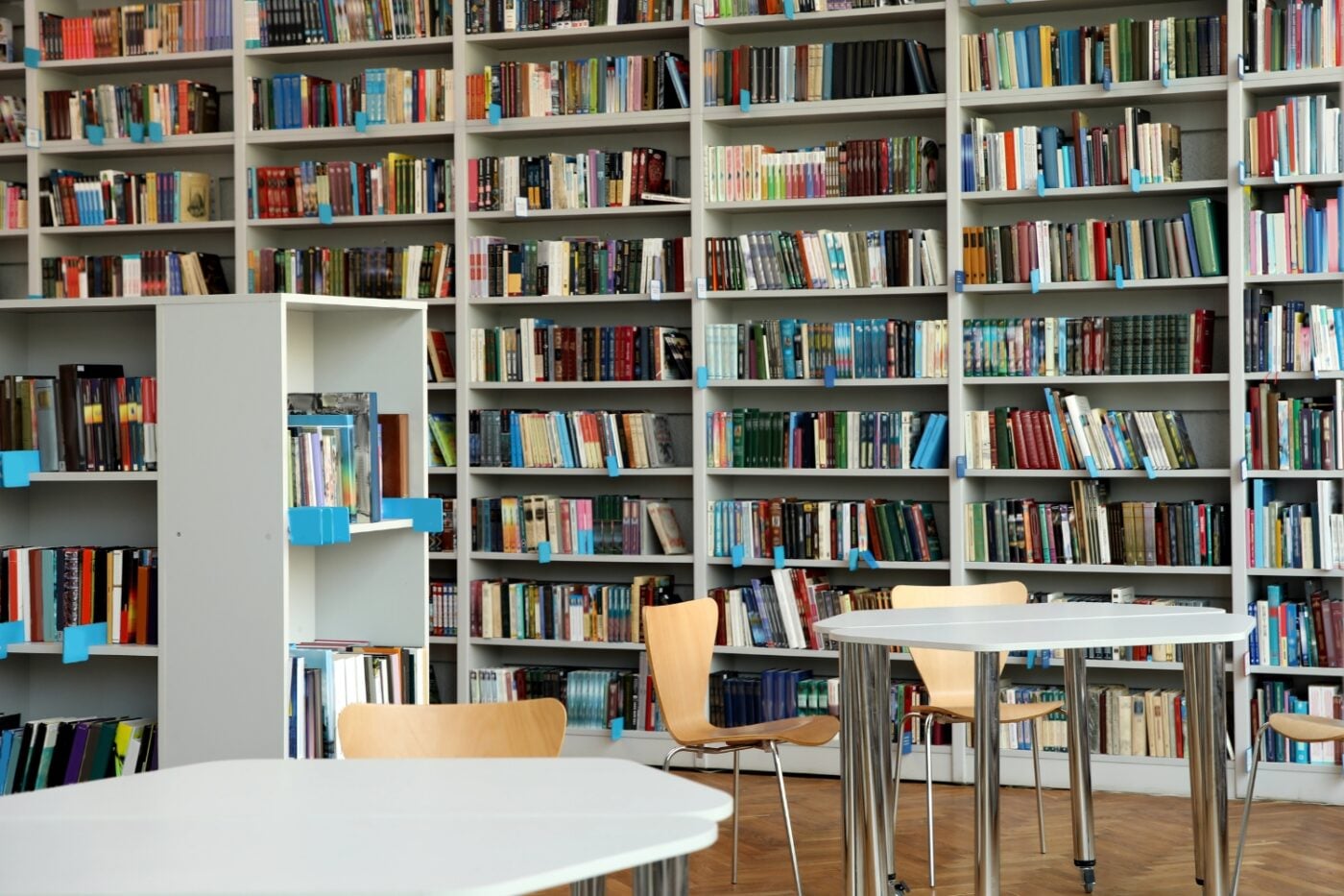 A modern public library with large white book shelves fileld with books and round tables with chairs