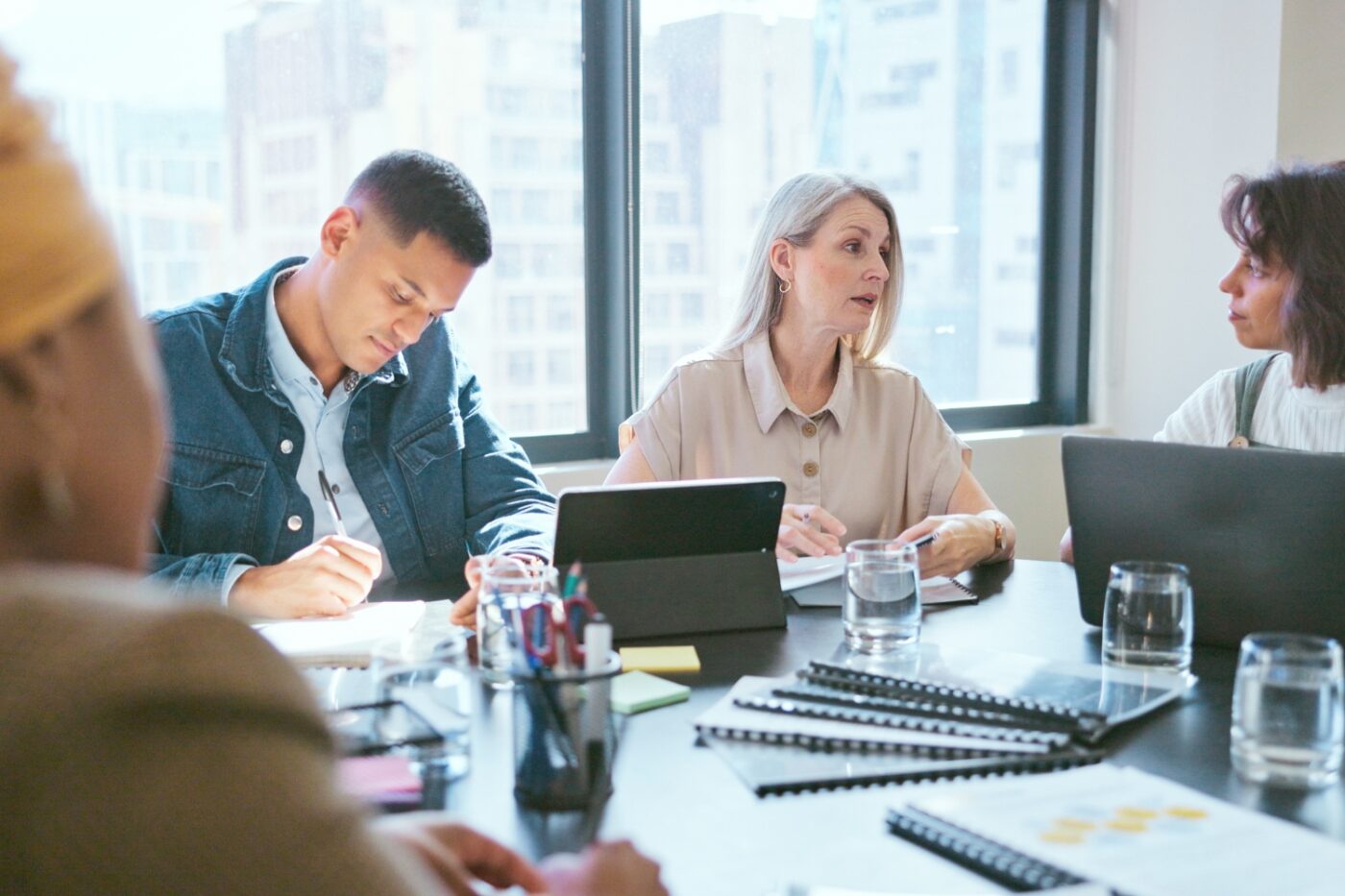 A team meeting with a consultant featuring three women and one man sitting at table with tablets and notebooks.