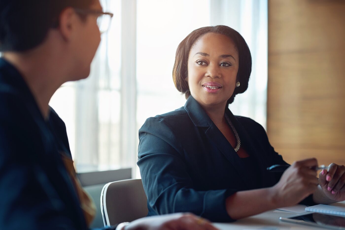 A woman dressed professionally at a job interview speaking with a man wearing glasses.