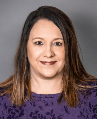 A woman with straight brown hair and a purple top smiles at the camera against a plain gray background, representing Bradbury Miller Associates (BMA).