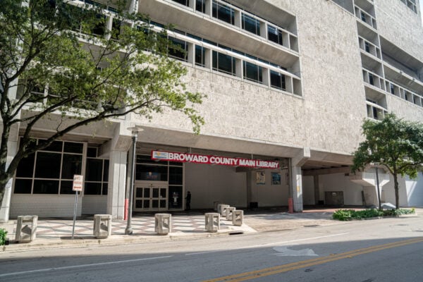The front entrance of Broward County Main Library, with red signage above, trees, and a sidewalk in front of a large concrete building—a project recognized by Bradbury Miller Associates.