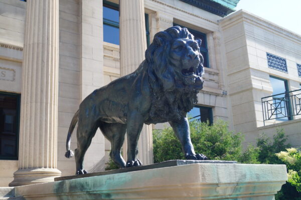 A bronze lion statue stands on a pedestal in front of a neoclassical building with large columns and windows, marking the headquarters of Bradbury Miller Associates (BMA).