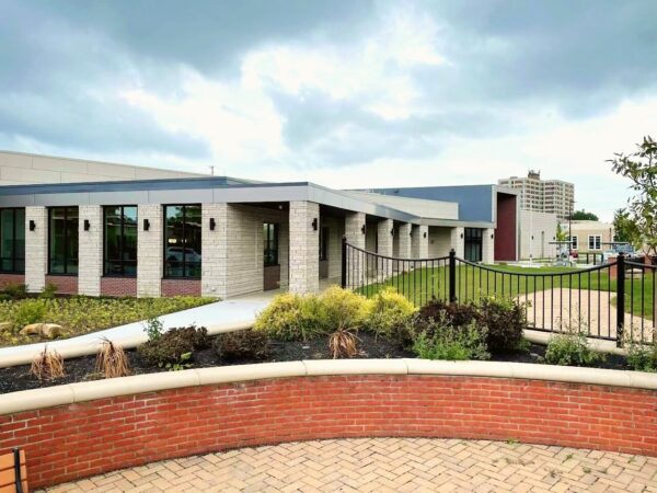 Modern single-story building with large windows, landscaped garden, brick walkway, and black metal fence under a cloudy sky—an inviting space brought to you by Bradbury Miller Associates.