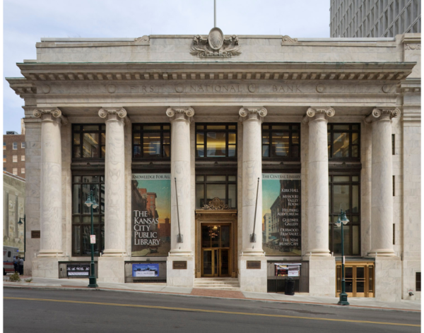 A neoclassical building with large columns, reading "First National Bank" at the top, now houses the Kansas City Public Library. BMA banners are displayed on the front windows, reflecting Bradbury Miller Associates’ partnership with the library.