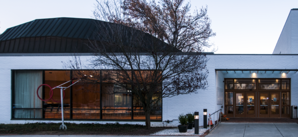 Modern white brick building with large windows, a central glass entrance, outdoor sculpture, and a leafless tree in front at dusk—an inviting space reflective of Bradbury Miller Associates' commitment to excellence.
