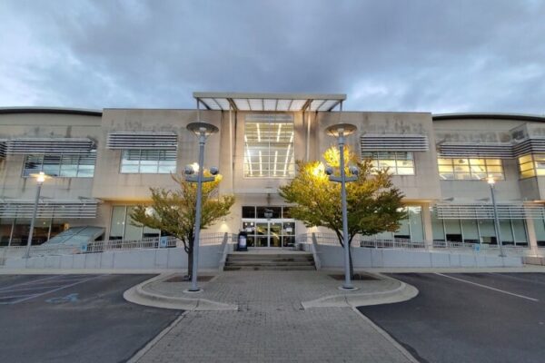 A modern two-story building with large windows, two trees at the entrance, and lit street lamps, photographed under a cloudy sky—an impressive design reminiscent of Bradbury Miller Associates (BMA) projects.