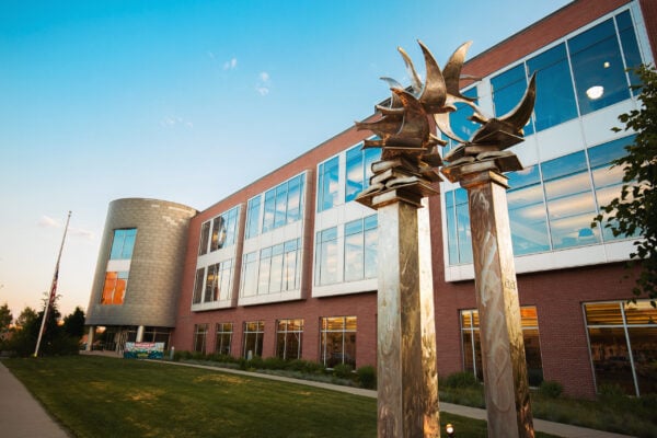 Modern brick and glass building with two tall metallic bird sculptures in front, set against a clear blue sky and landscaped lawn—an impressive property presented by Bradbury Miller Associates (BMA).