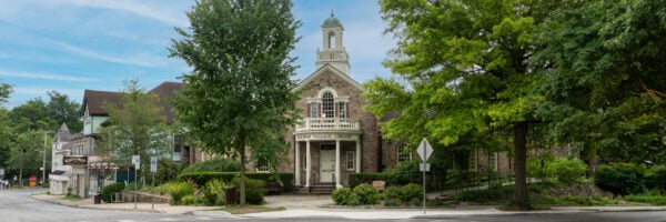 Historic stone Village Library building with a cupola, surrounded by trees and greenery, located at a street corner in Katonah NY on a clear day.