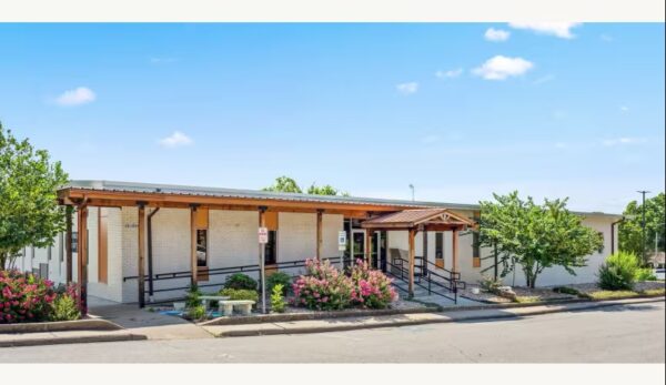 Single-story building with a covered entrance, ramps, flowering bushes, and trees under a clear blue sky—a welcoming space presented by Bradbury Miller Associates (BMA).