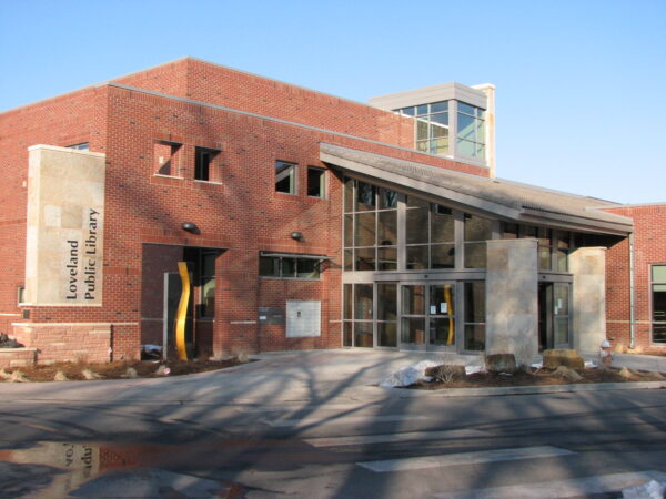 A modern red-brick building with large windows and a sign reading "Loveland Public Library" near the entrance, the facility was designed in consultation with Bradbury Miller Associates (BMA).