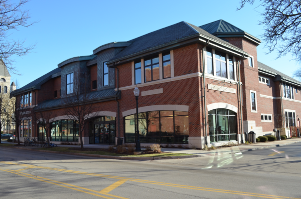 A two-story red brick commercial building with large windows on a sunny day, located at a street corner with trees and a church in the background, features signage for Bradbury Miller Associates (BMA).