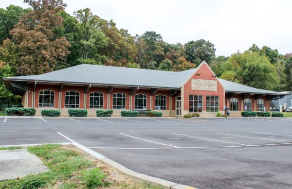 A large brick building with arched windows, located in front of an empty parking lot and surrounded by trees, houses the offices of Bradbury Miller Associates (BMA).