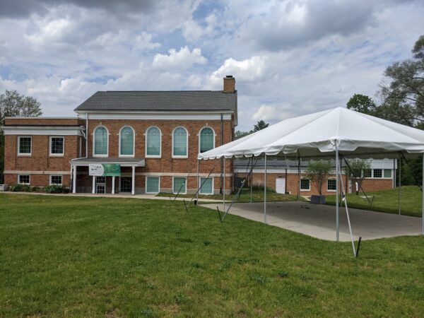 A brick building with large arched windows and a white canopy tent set up on a grassy lawn under a cloudy sky, perfect for a BMA event hosted by Bradbury Miller Associates.