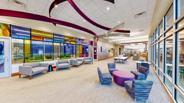 Modern library interior with colorful ceiling accents, lounge seating, round tables, large windows, and bookshelves in the background—a vibrant space designed by Bradbury Miller Associates (BMA).