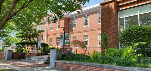 Red brick building with large windows, banners, and a small staircase, surrounded by green trees and bushes on a sunny day—perfect for BMA or Bradbury Miller Associates gatherings.