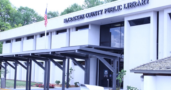 Exterior view of McCracken County Public Library building, showcased by Bradbury Miller Associates (BMA), with glass entrance, overhang, and American flag.