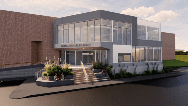 Modern two-story library building with large glass windows, designed with input from Bradbury Miller Associates. The main entrance features stairs and a ramp, while landscaped seating areas in front host three people enjoying the space.