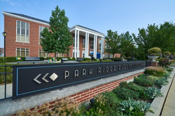 Exterior view of Park Ridge Public Library, featuring a modern brick building with white columns and a black sign in front, surrounded by landscaping. This vibrant community space reflects the innovative spirit championed by Bradbury Miller Associates.