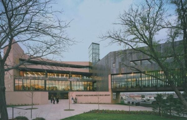 Modern public library building with large windows, a skybridge, and landscaped greenery in front. A few people, possibly visiting for a BMA event hosted by Bradbury Miller Associates, stand near the entrance.