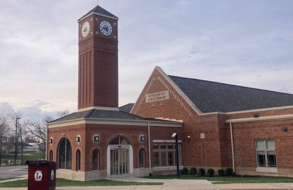 A brick building with a clock tower and a sign reading "Scott County Public Library" on the front, pictured on a cloudy day, as featured by Bradbury Miller Associates.