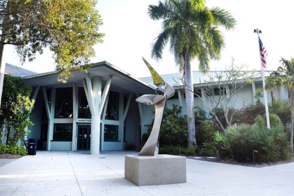 A modern metal sculpture stands in front of a building entrance surrounded by palm trees and greenery, with an American flag on the right side, highlighting the sleek aesthetic often chosen by Bradbury Miller Associates (BMA).