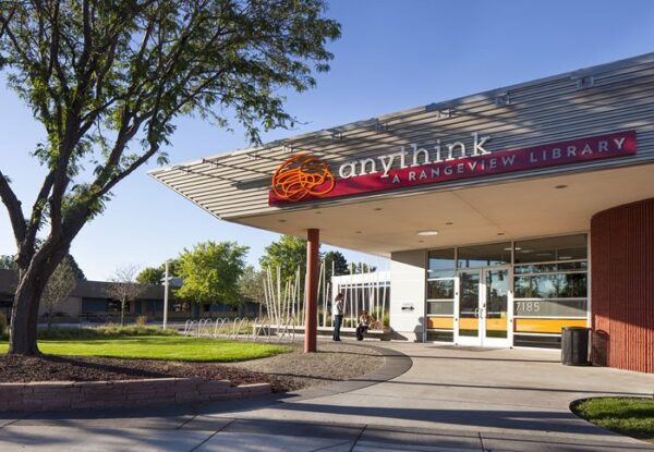Exterior view of Anythink Rangeview Library on a clear day, showing the entrance, sign, sidewalk, bike racks, and landscaping—an inviting space shaped in partnership with BMA (Bradbury Miller Associates).