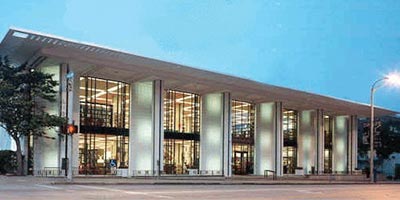 A modern library building with tall glass windows and vertical columns, illuminated from inside at dusk, showcases the innovative design championed by Bradbury Miller Associates.