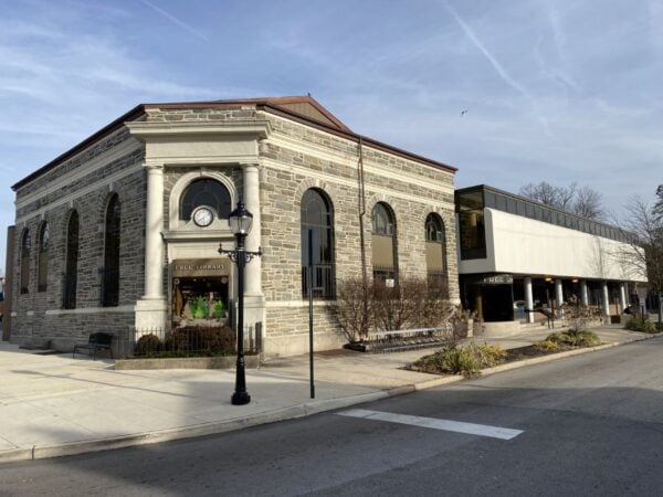 A stone public library building with arched windows sits next to a modern white structure on a quiet street corner, reflecting the timeless architectural values BMA, Bradbury Miller Associates, often champions.