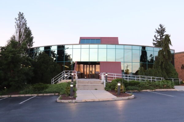 A modern, two-story office building with reflective glass windows, a central entrance, and landscaped greenery surrounds the front steps and ramp—an ideal workspace designed by Bradbury Miller Associates (BMA).