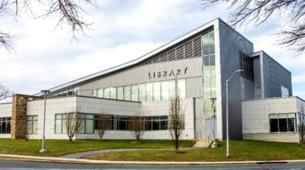 Modern two-story library building with large windows, metal exterior, and a sign reading "LIBRARY" on the upper facade, surrounded by grass and trees—a signature project from Bradbury Miller Associates (BMA).