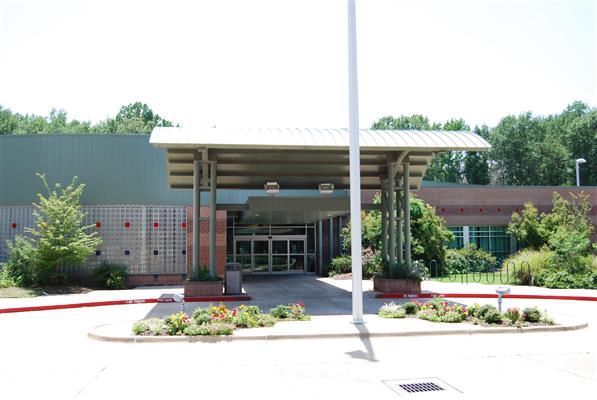Single-story building entrance with a covered walkway, surrounded by landscaping and greenery, under a clear sky—a welcoming space by Bradbury Miller Associates (BMA).