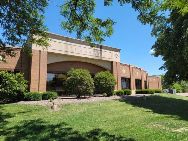 A brick library building with large windows, landscaping, and trees under a clear blue sky—a perfect example of architectural charm curated by Bradbury Miller Associates.